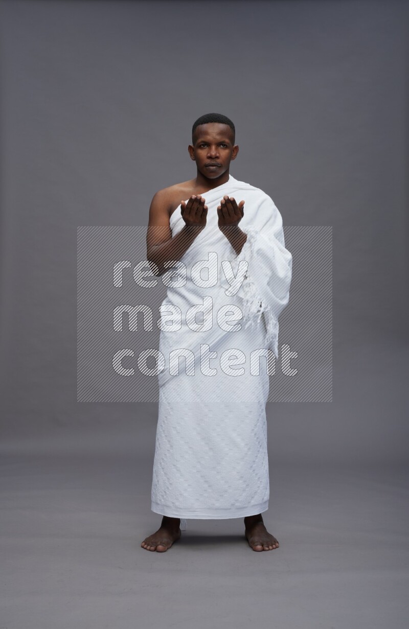A man wearing Ehram Standing dua'a on gray background