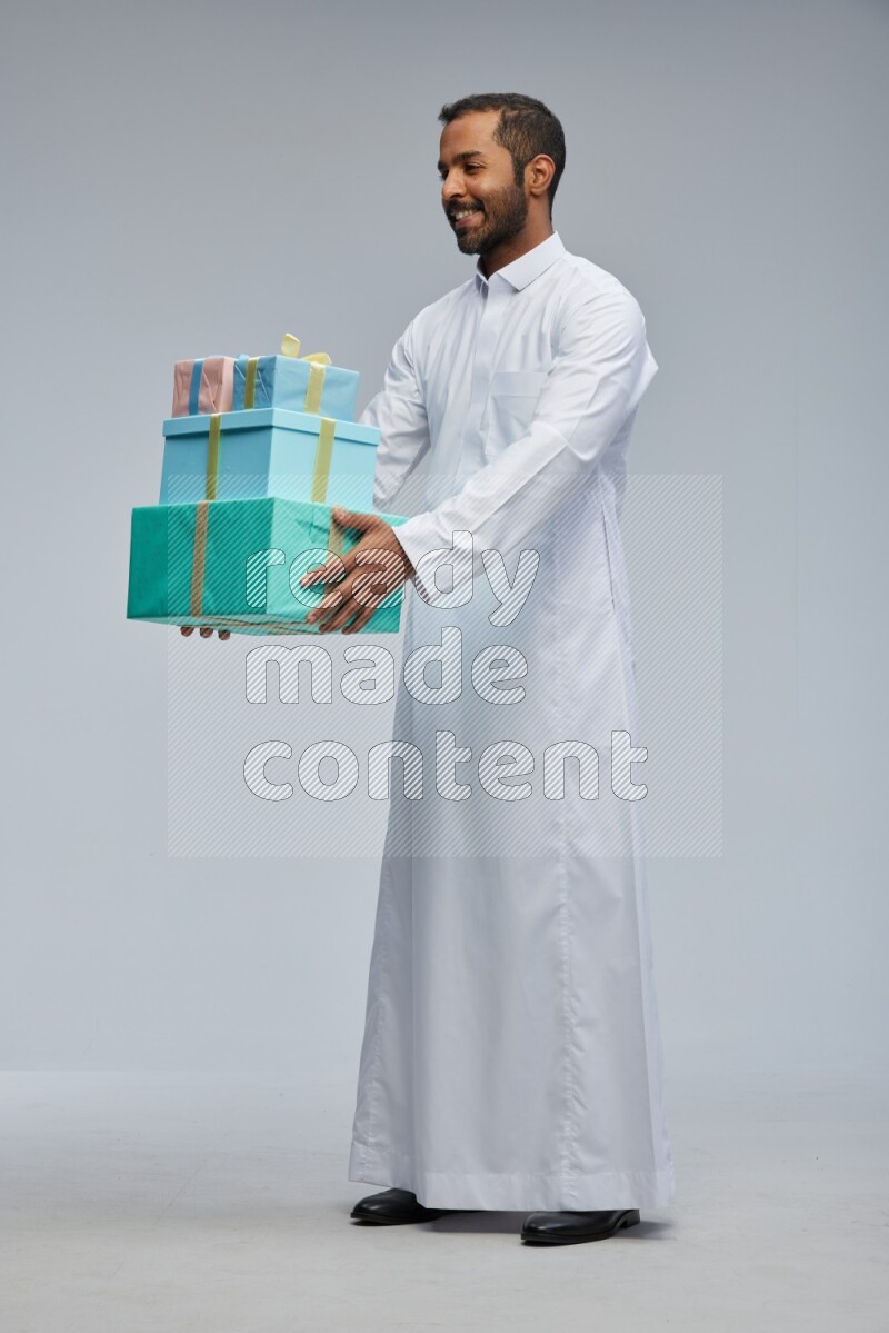 Saudi man Wearing thob standing holding gift box on Gray background