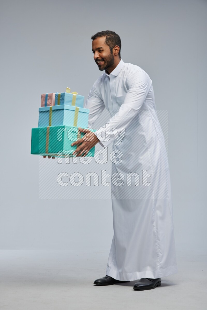 Saudi man Wearing thob standing holding gift box on Gray background