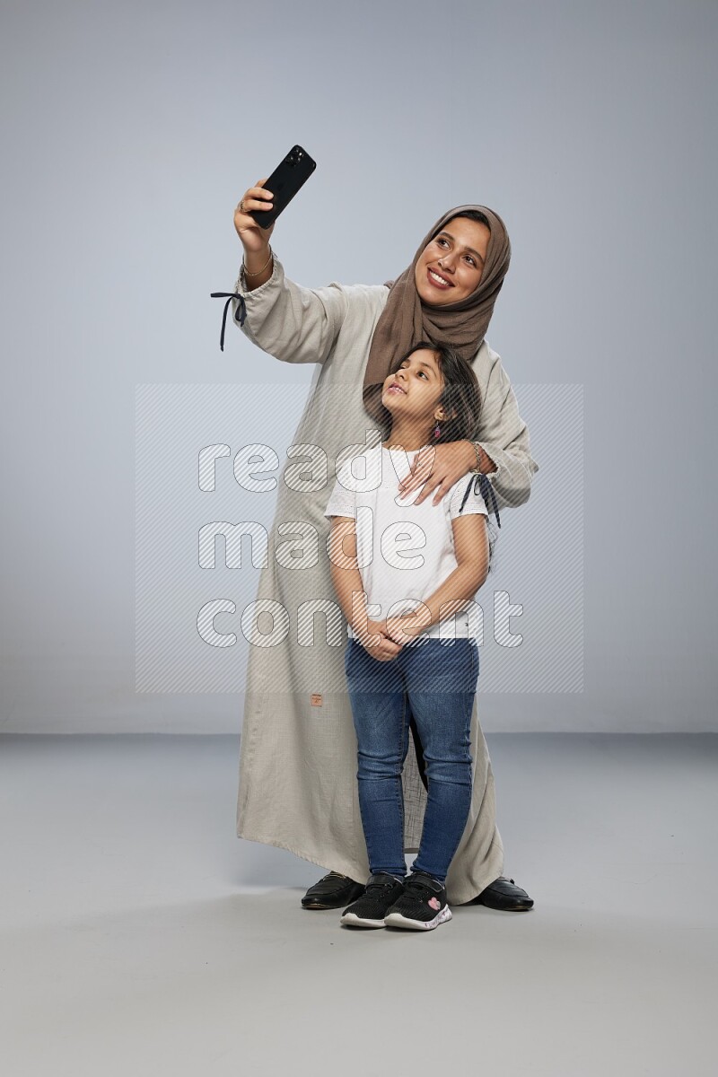 A girl standing taking selfie with her mother on gray background