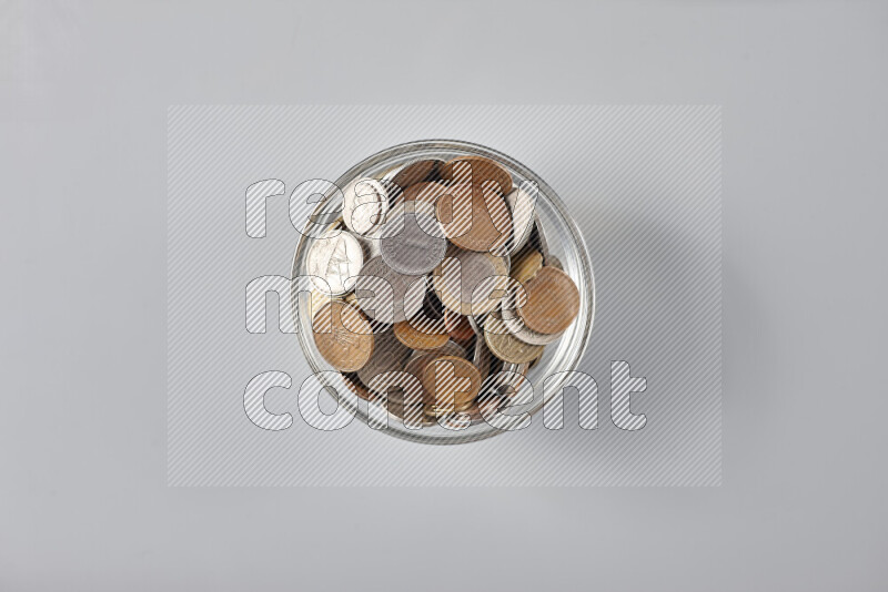 Random old coins in a glass bowl on grey background