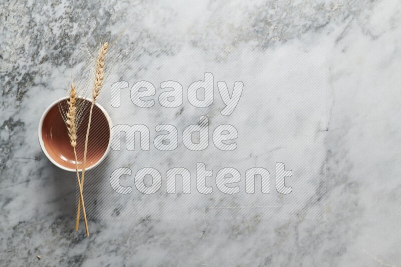 Wheat stalks on brown pottery bowl on grey marble background