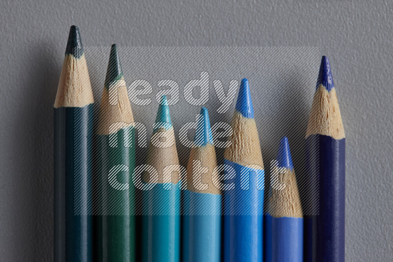 A collection of colored pencils arranged showcasing a gradient of blue hues on grey background