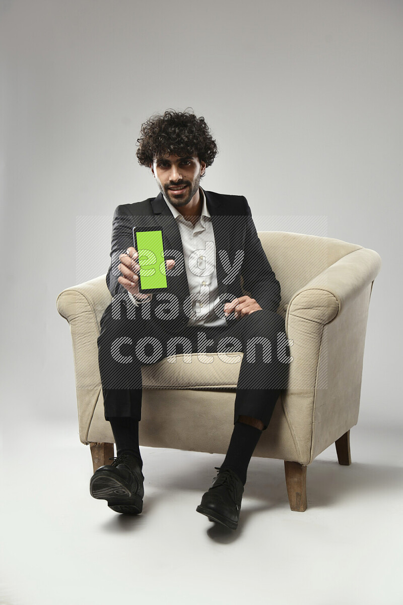 رجل يرتدي ملابس رسمية يجلس علي كرسي و يحمل هاتف علي خلفية بيضاء