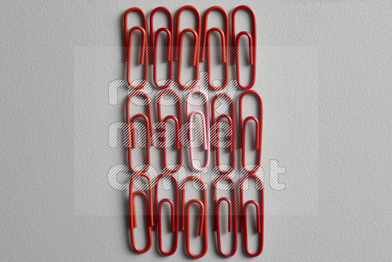 A pink paperclip surrounded by bunch of red paperclips on grey background