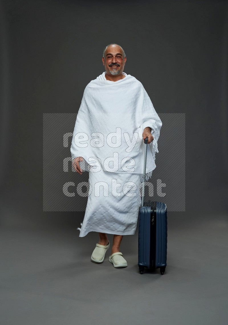 A man wearing Ehram Standing holding traveling bag on gray background