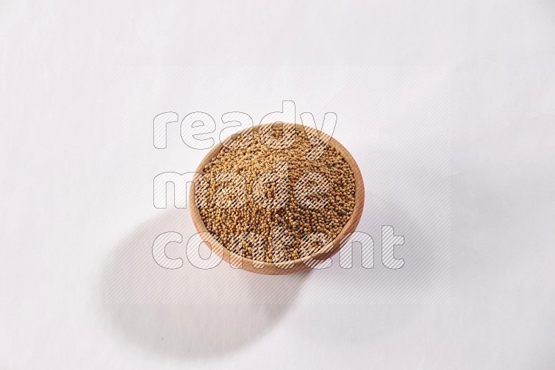 A wooden bowl full of mustard seeds on a white flooring