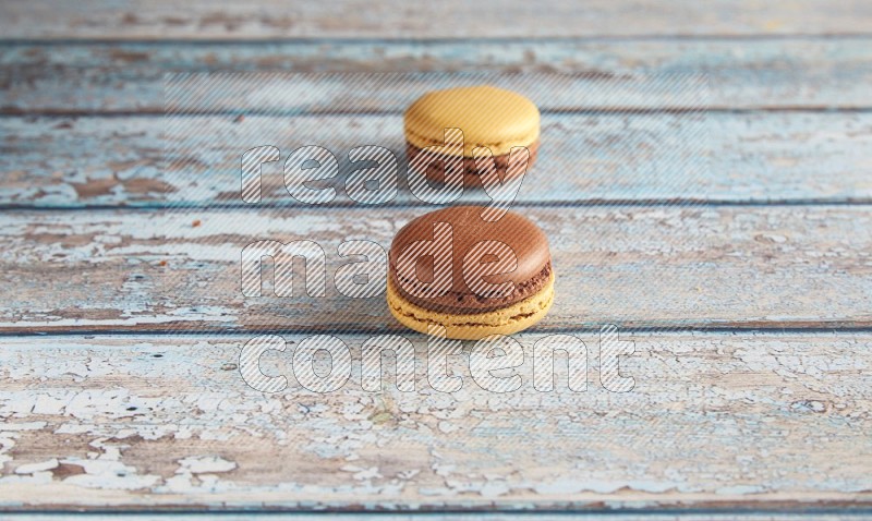 45º Shot of two Yellow and Brown Chai Latte macarons on light blue wooden background