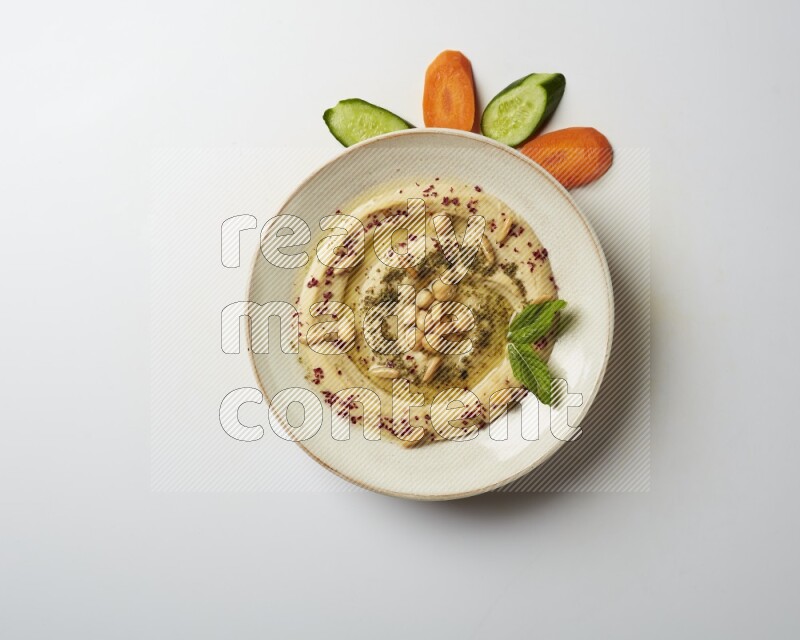 Hummus in a pottry plate garnished with zaatr & sumak on a white background