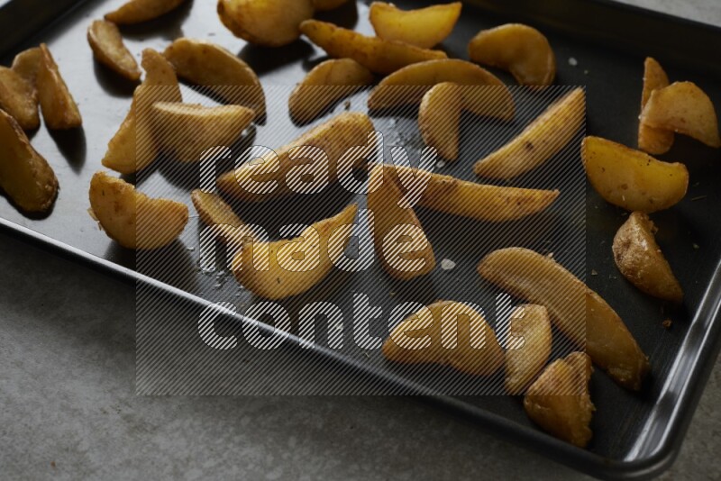 wedges potato in a black stainless steel rectangle tray on grey textured counter top