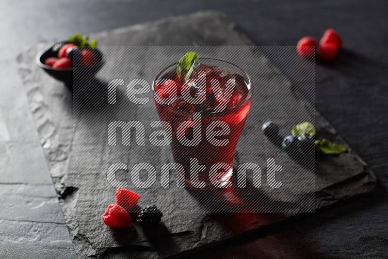 A glass of mixed berries juice with mint leaves on black background