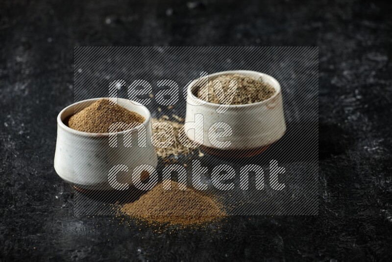 وعاءين بيج، أحدهما ممتلئ ببودرة الكمون والآخر ممتلئ بحبوب الكمون، على خلفية سوداء