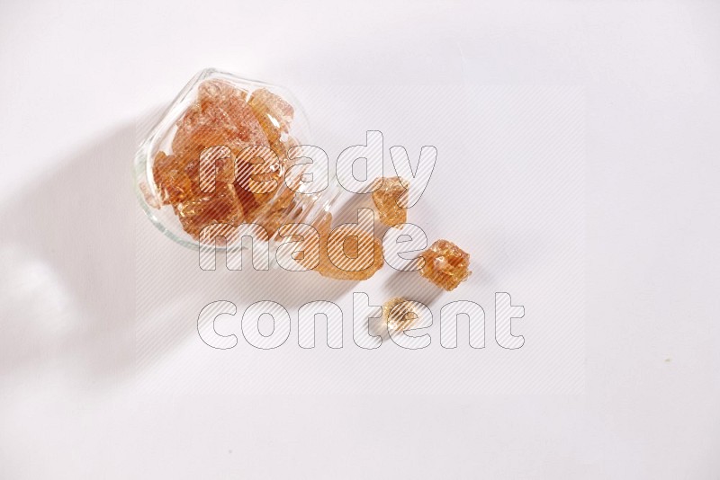 A glass spice jar full of gum arabic and jar is flipped with fallen gum arabic on white flooring in different angles