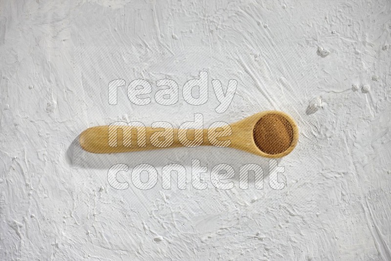 Cinnamon powder in a wooden spoon on a white background