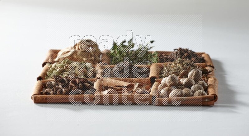9 squares of cinnamon sticks full of tea in the middle surrounded by nutmeg, dried mint, cloves, dried basil, dried ginger, cinnamon, star anise and cardamom on white flooring