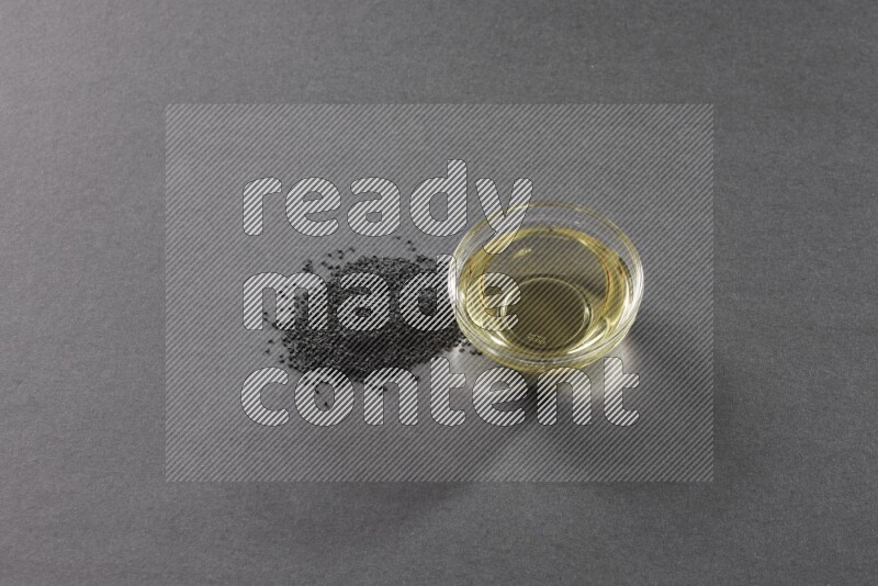 وعاء زجاجي ممتلئ بزيت حبة البركة مع بعض البذور بجانبه على أرضية سوداء