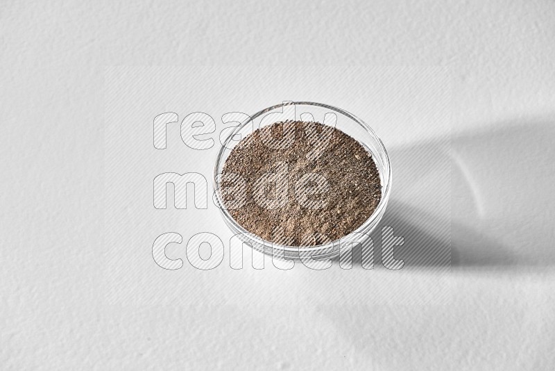 A glass bowl full of black pepper powder on white flooring