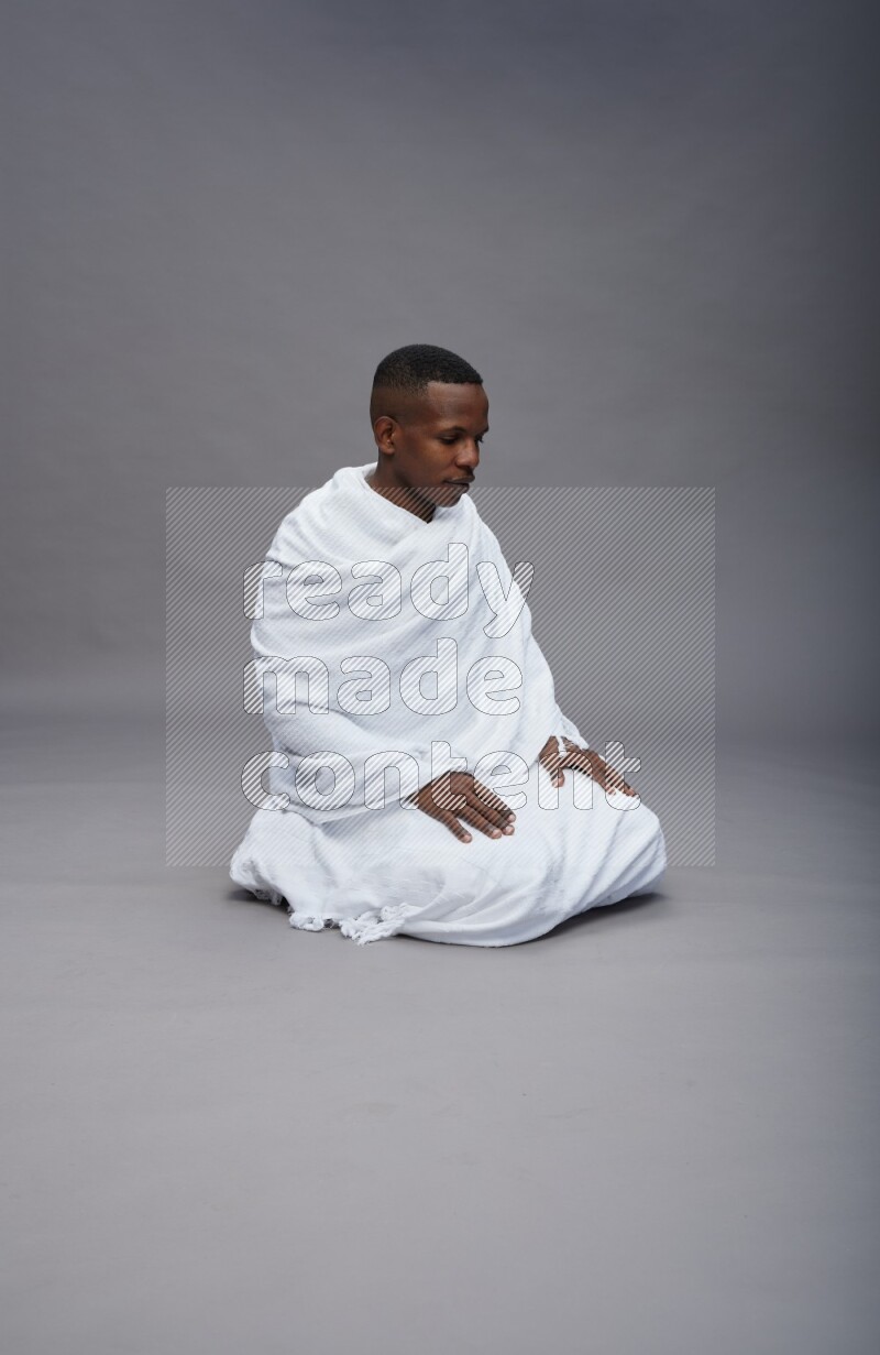 A man wearing Ehram sitting on floor praying on gray background