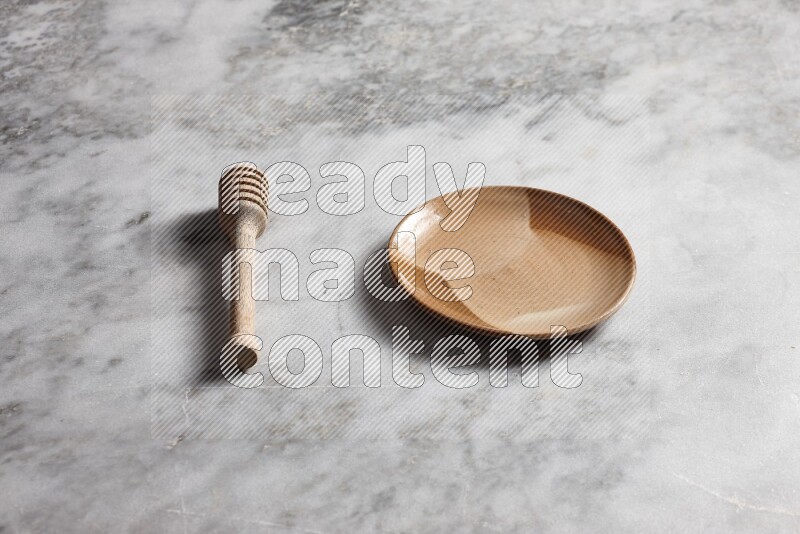 Multicolored pottery plate with wooden honey dipper on the side on grey marble background