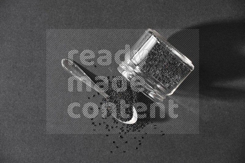A glass jar full of black seeds flipped and seeds spreaded out with a metal spoon full of the seeds on a black flooring in different angles