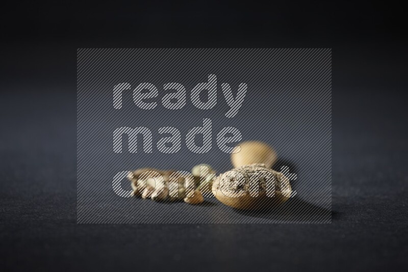 ملعقة خشبية ممتلئة ببودرة الهيل وحبوب الهيل بجانبها على خلفية سوداء