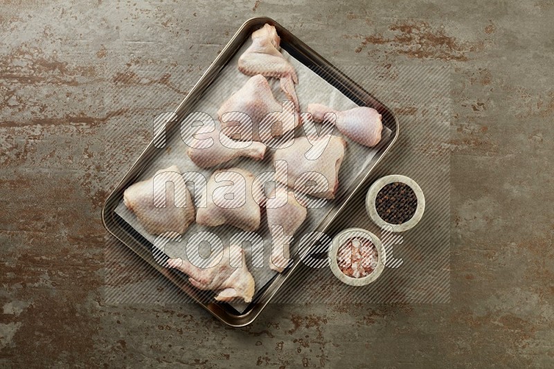 Mixed fresh chicken pieces in an oven tray on a textured rustic background