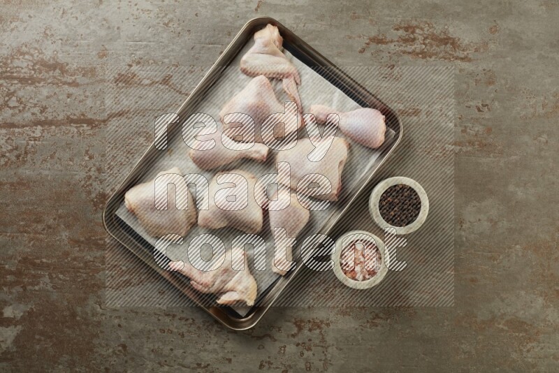 Mixed fresh chicken pieces in an oven tray on a textured rustic background
