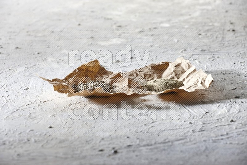 White pepper beads and powder in crumpled pieces of paper on textured white flooring