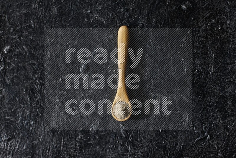 ملعقة خشبية مليئة ببودرة الفلفل الأبيض على أرضية سوداء