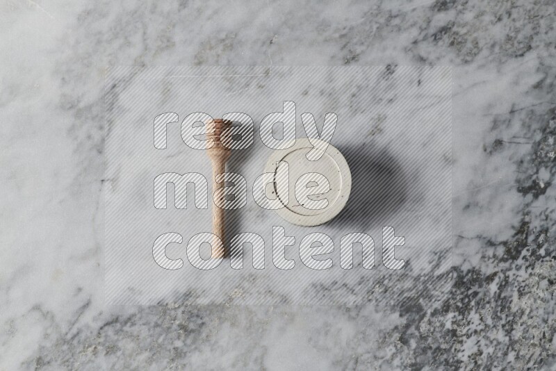 White pottery bowl with wooden honey dipper on the side on grey marble background
