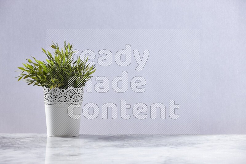Green artificial plant in white decorative pot on grey marble background