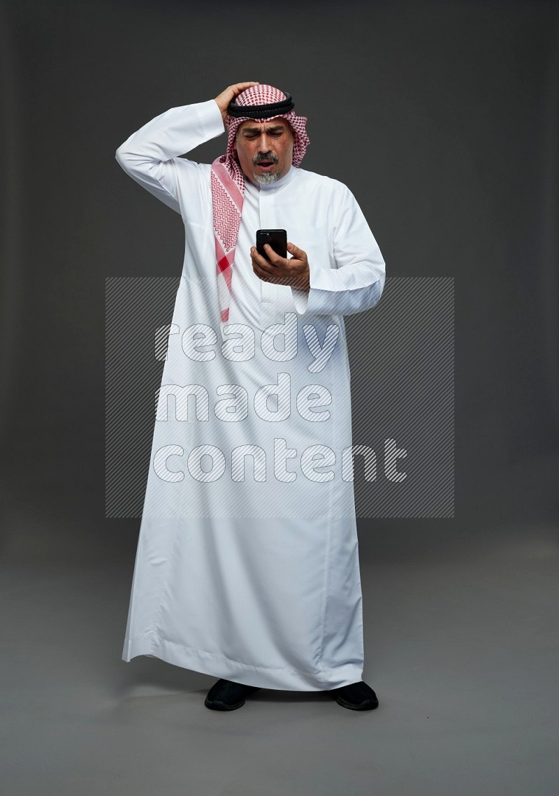 Saudi man with shomag Standing texting on phone on gray background