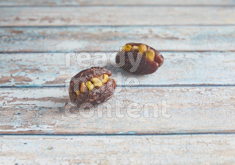 two pistachio stuffed madjoul dates on a light blue wooden background