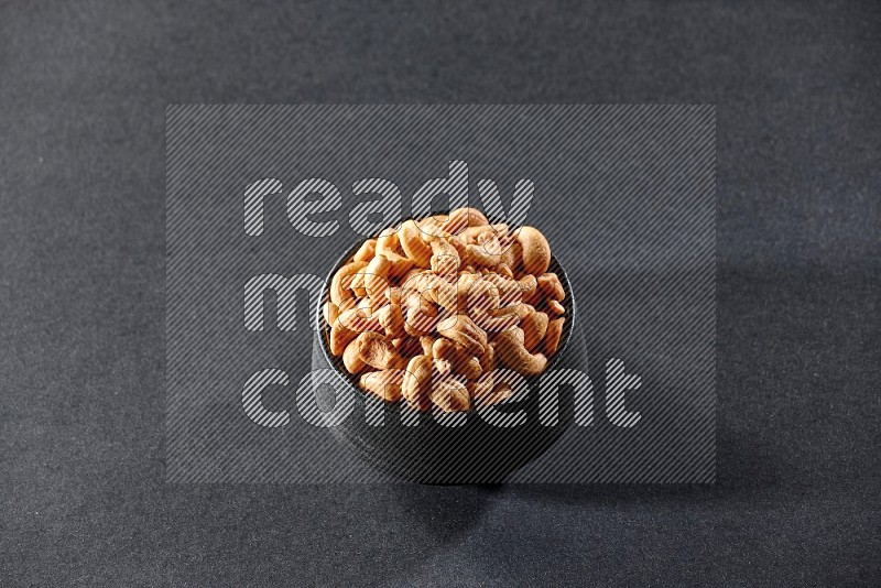 A black pottery bowl full of cashews on a black background in different angles