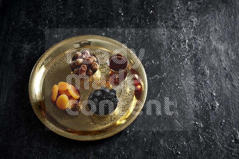 Dried fruits in metal bowls on a tray in a dark setup