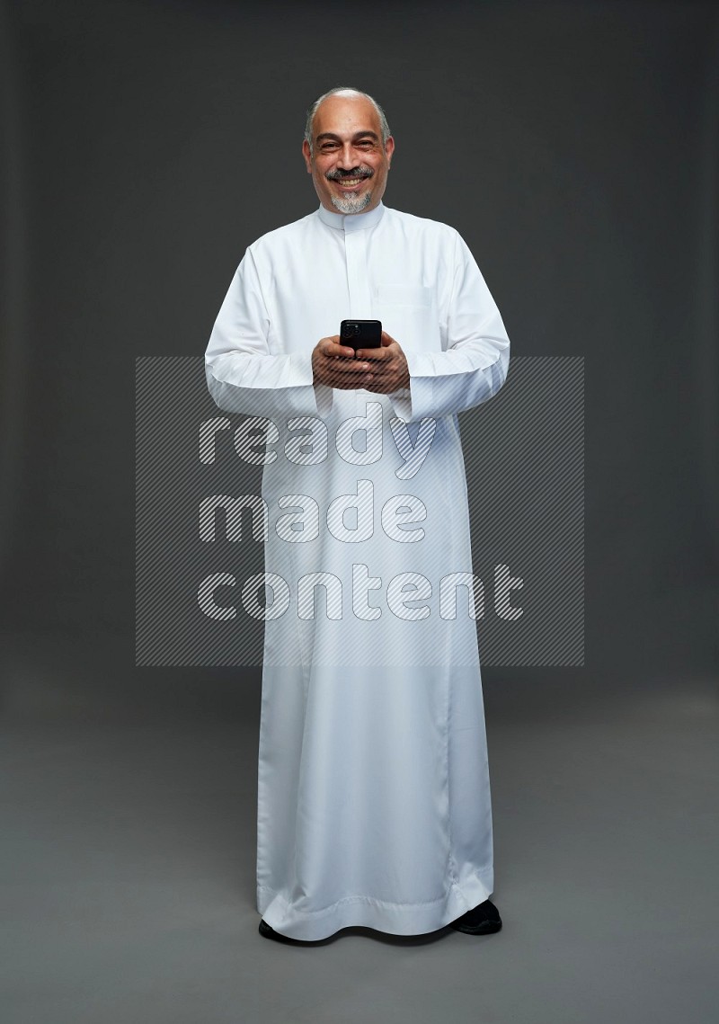 Saudi man without shomag Standing texting on phone on gray background