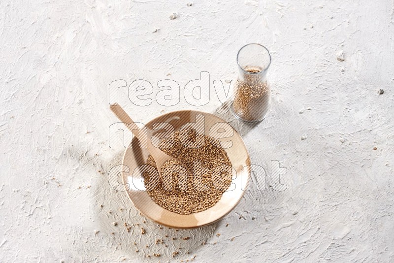 صحن فخار بيج ممتلئ ببذور الخردل وملعقة خشبية ممتلئة داخله مع وعاء زجاجي ممتلئ ببذور الخردل على خلفية بيضاء