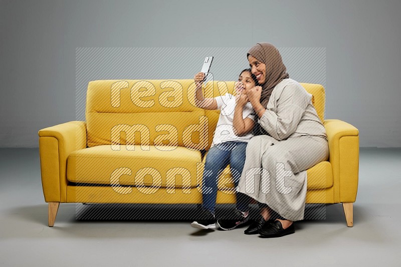 A girl sitting taking selfie with her mother on gray background