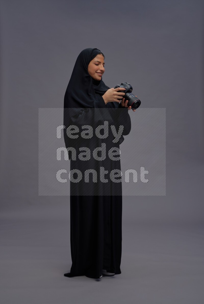 Saudi woman wearing Abaya standing holding Camera on gray background