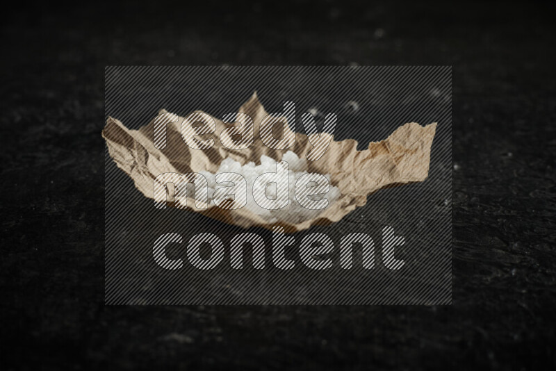 A crumpled piece of paper full of white salt on black background