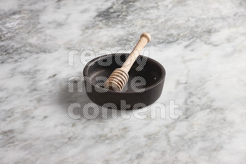 Black Pottery Oven Plate with wooden honey handle in it, on grey marble flooring, 45 degree angle