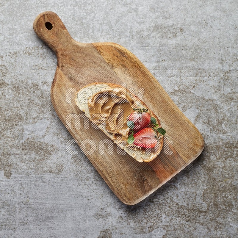 open faced peanut butter sandwich with strawberries on a grey textured background
