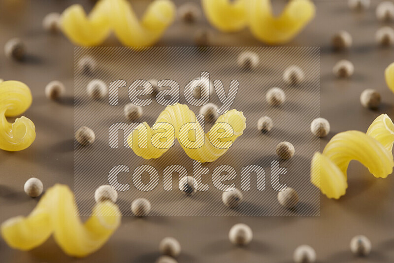 Raw pasta with different ingredients such as cherry tomatoes, garlic, onions, red chilis, black pepper, white pepper, bay laurel leaves, rosemary and cardamom on beige background