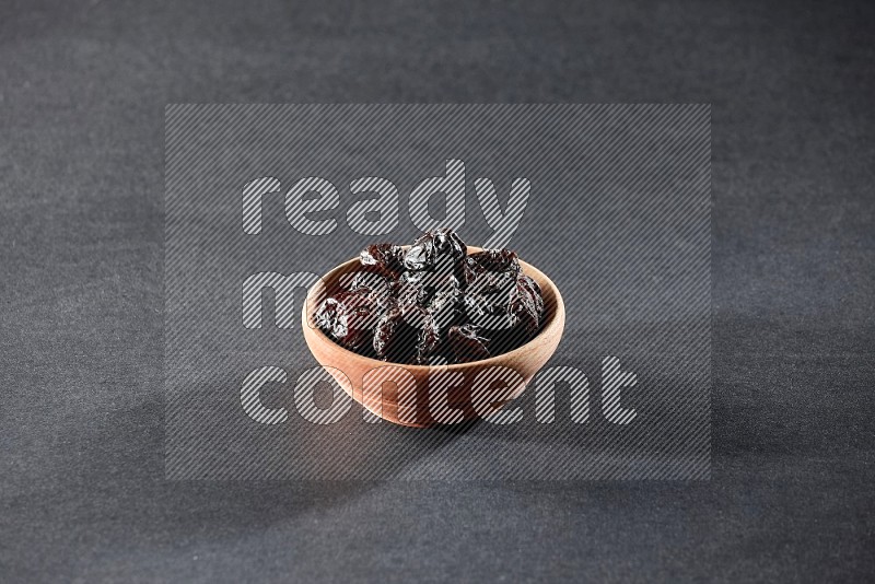 A wooden bowl full of dried plums on a black background in different angles