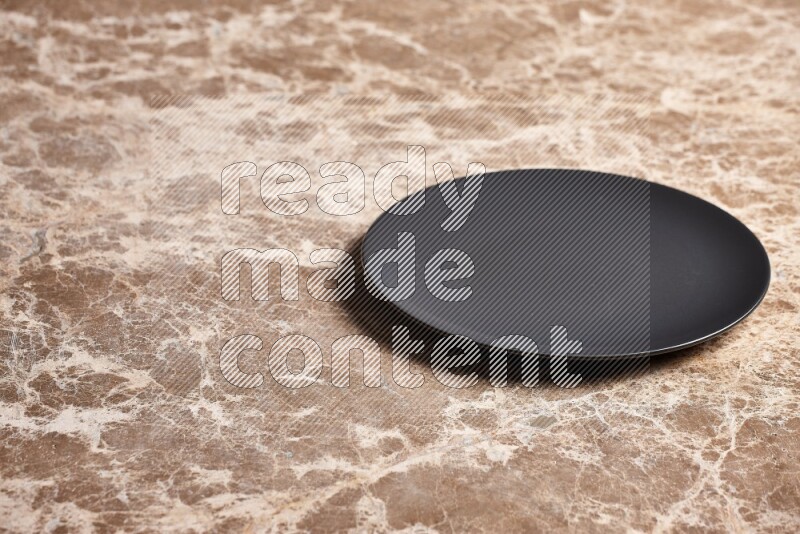 A black ceramic circular plate on beige marble background