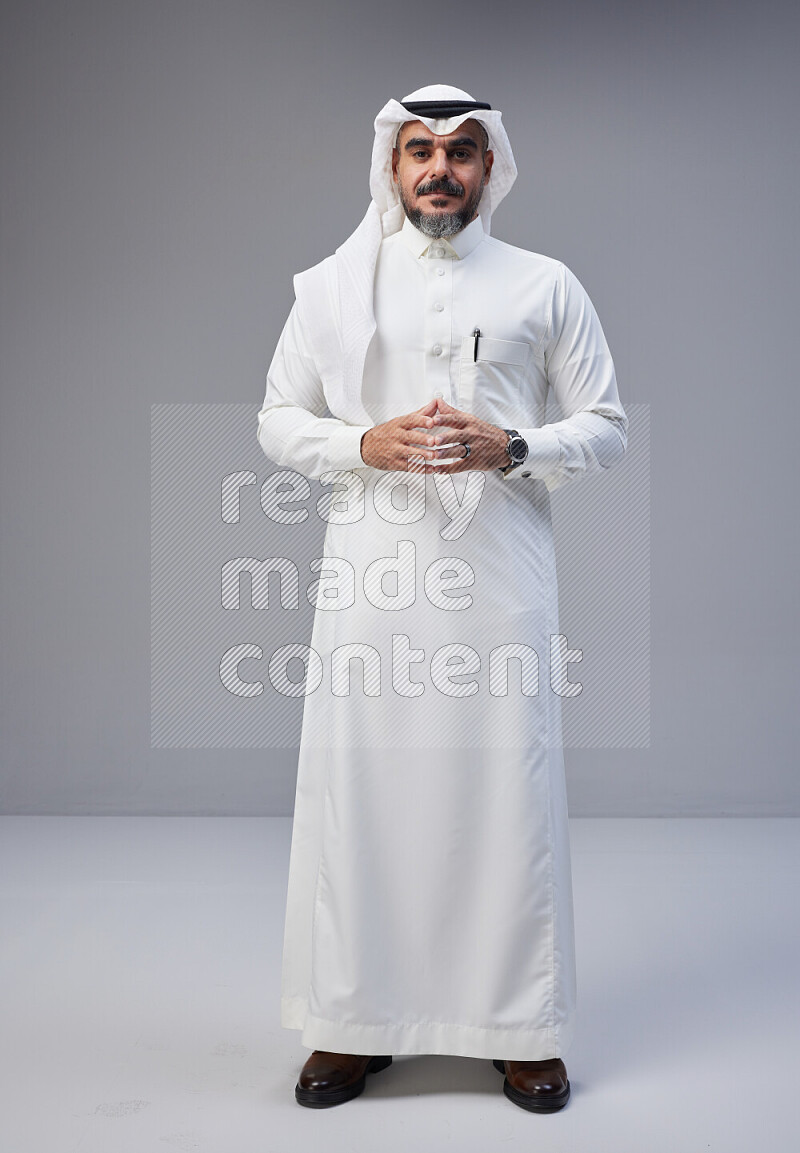 Saudi man Wearing Thob and white Shomag standing interacting with the camera on Gray background