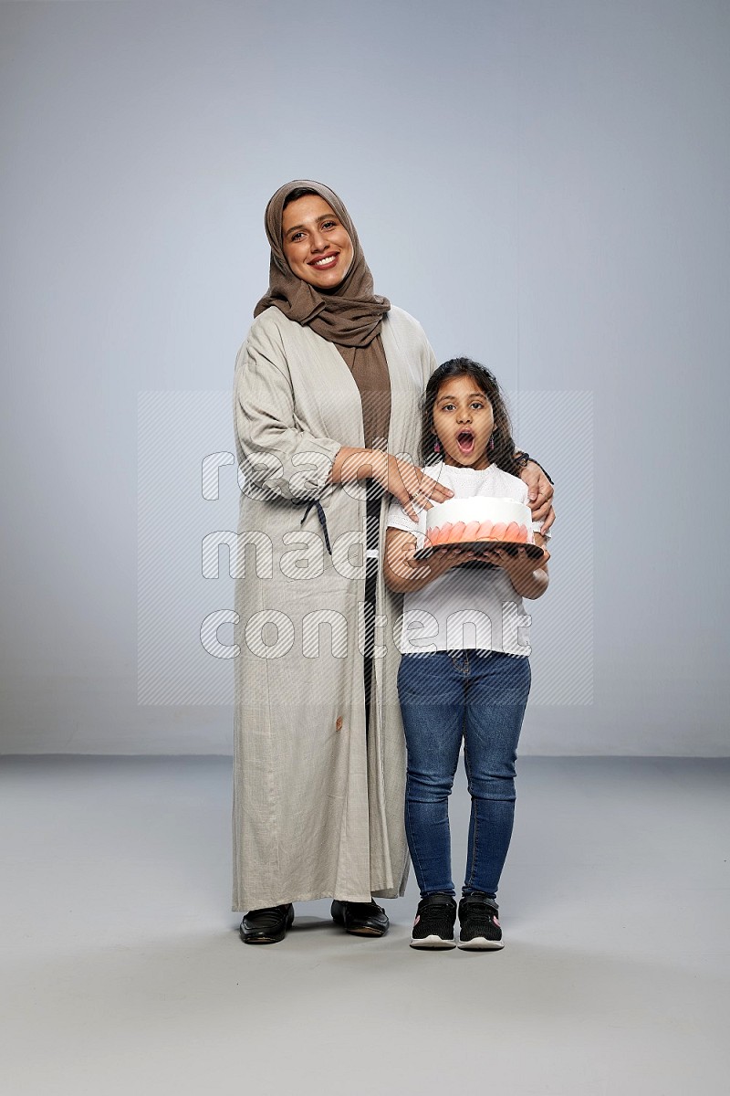 A girl giving a cake to her mother on gray background