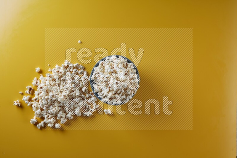 A blue pottery bowl full of popcorn with popcorn beside it on a yellow background in different angles