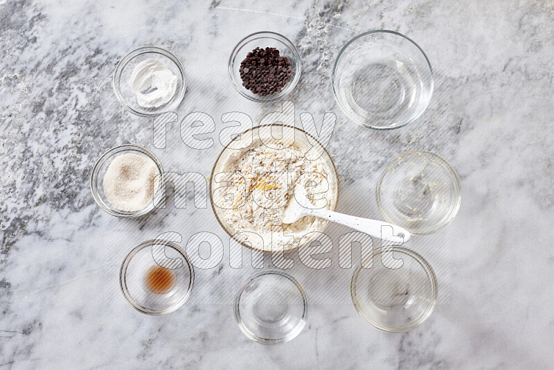 Cookies step by step with its ingredient, flour, butter, brown sugar, egg, vanilla extract, white sugar, chocolate chips and baking soda on grey marble background