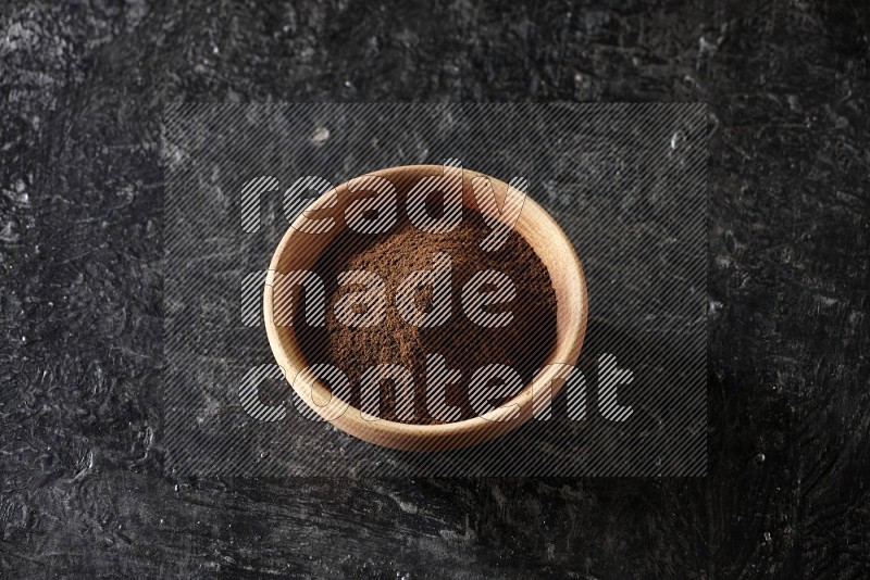 A wooden bowl full of cloves powder on a textured black flooring